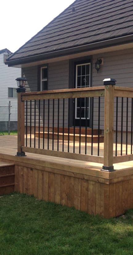 Wooden deck with metal balusters and wooden handrails next to a house.