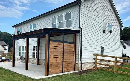 Wooden pergola attached to the side of a modern house with a small patio area.