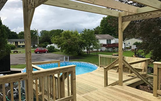Wooden deck with railing overlooking a backyard pool.